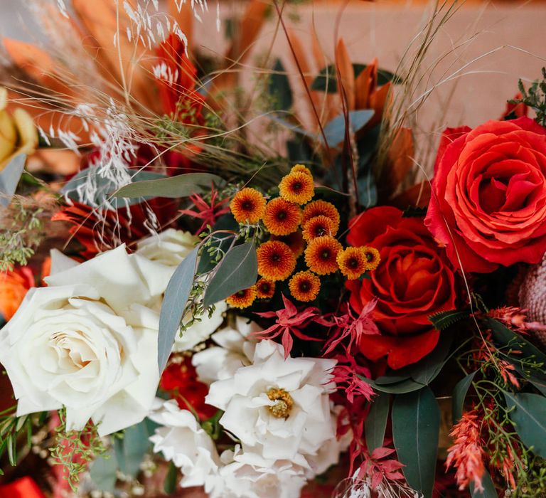 Mixed colourful wedding florals with roses and dried grasses in reds, oranges and greens