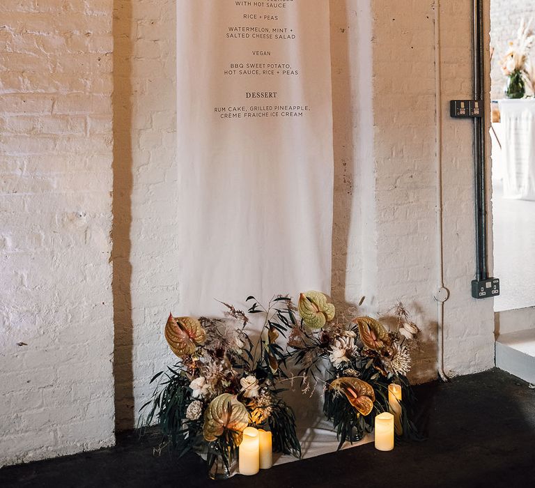 Large hanging fabric menu sign with flower arrangement at the footer 