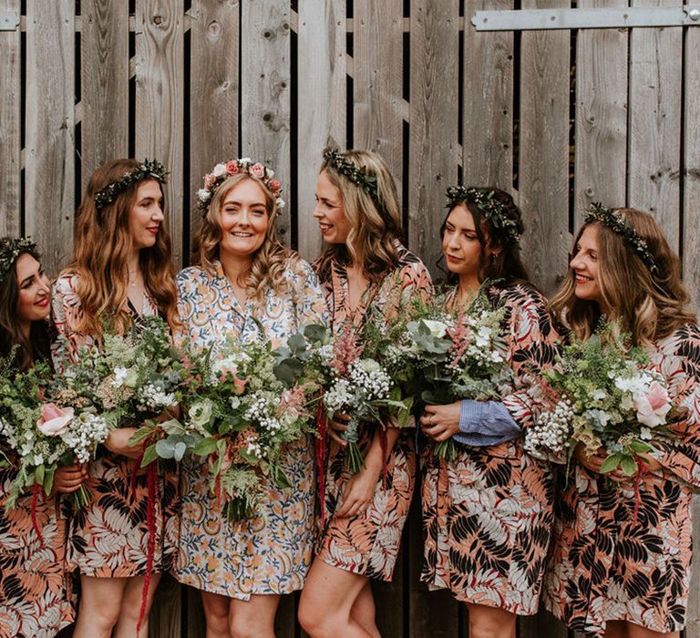 Bride in flower crown with bridesmaids in patterned robes holding rose, gypsophila and other flower wedding bouquets on the morning of the wedding 