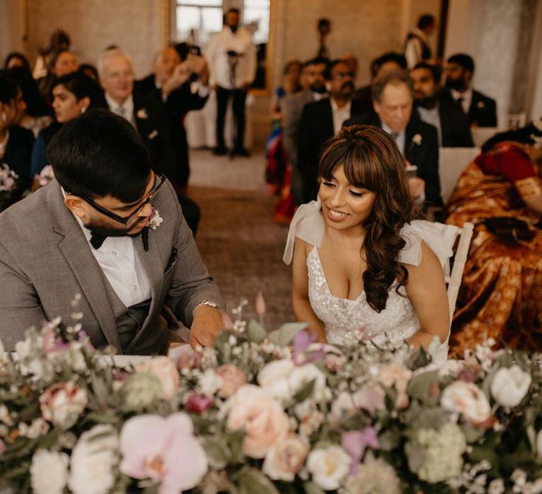 Bride and groom sitting at their wedding in front of large mixed neutral and green floral display 