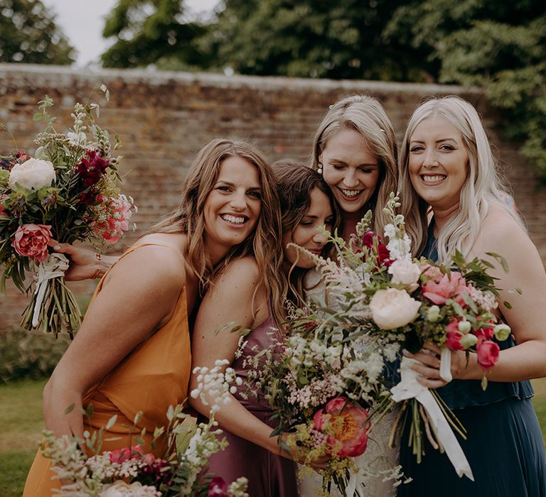 Bride hugs her bridesmaids holding pink and white and red bouquets