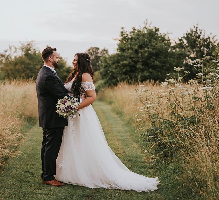 Groom holds the bride around her waist as they stand together in the grounds of Micklefield Hall