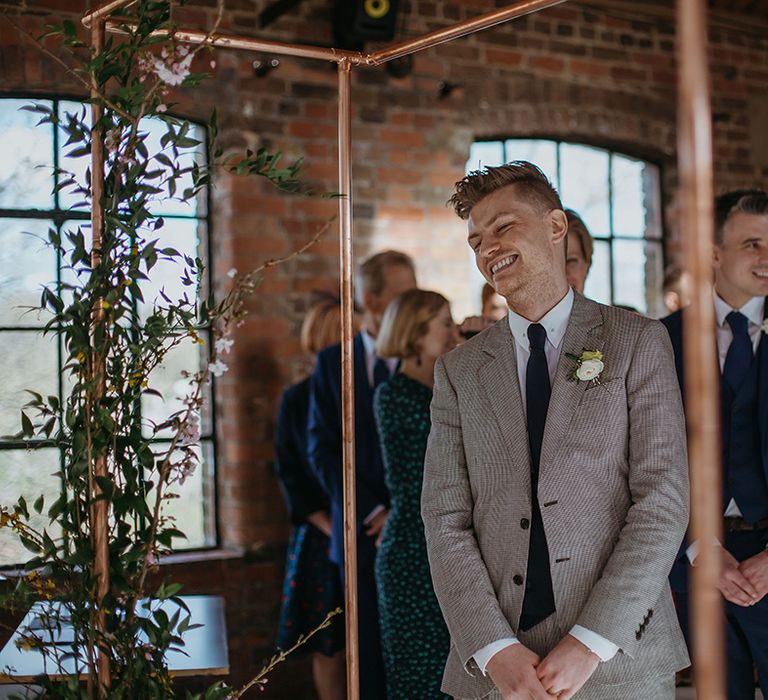 Groom in puppytooth suit and navy blue tie smiles as he hears the Jurassic Park entrance theme music