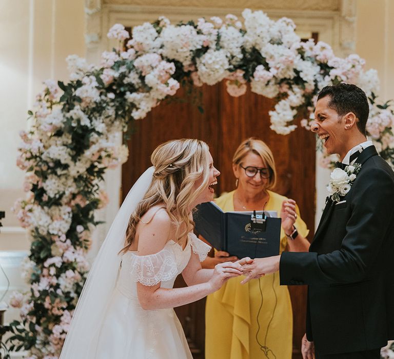 Bride and groom laugh as the bride puts on the groom's wedding ring 