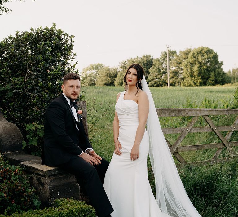 Bride in a Madi Lane one shoulder wedding dress poses with the groom in black tie for their hybrid style wedding 