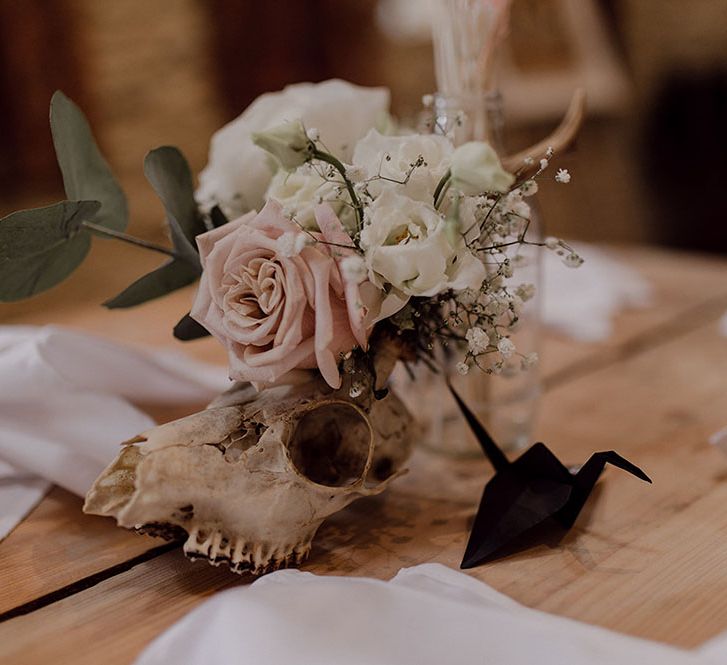 Skull decor beside small florals featuring pink rose on wooden table 