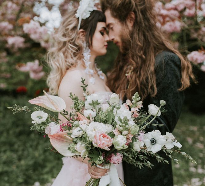 Couples' portrait under a blossom tree with bride holding a pink and white Spring wedding bouquet with anthuriums 