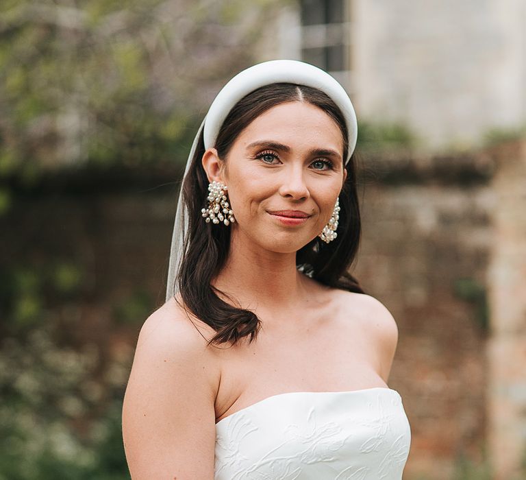 Bride in a strapless brocade wedding dress with a chunky white headband and statement pearl earrings 