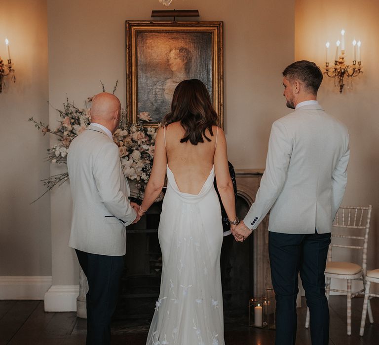 Bride in low back satin wedding dress standing at the altar at Iscoyd Park with her father and the groom 