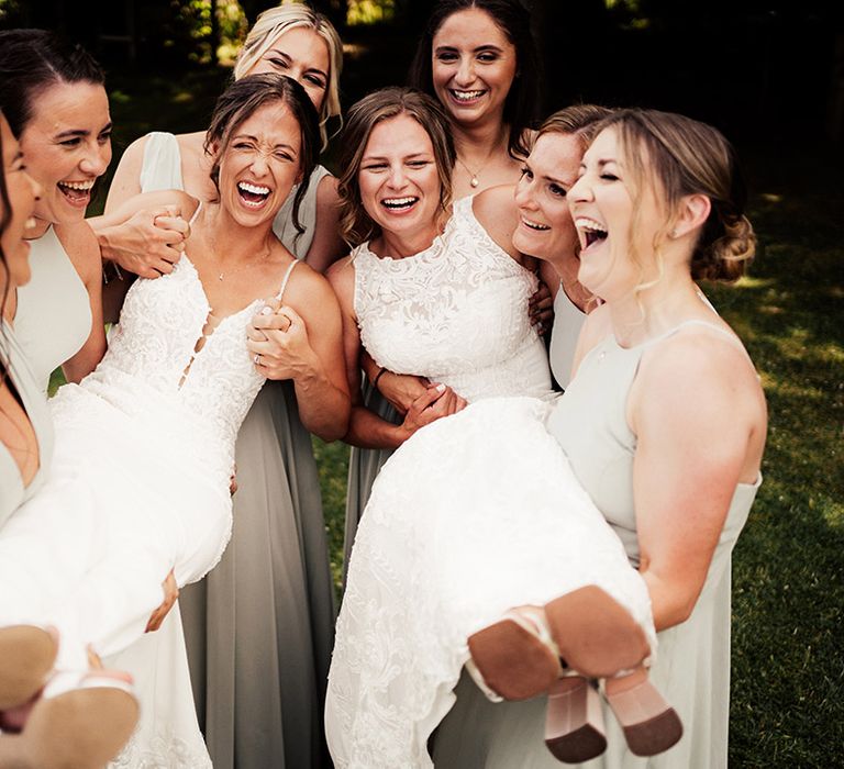 Bridesmaids in soft green bridesmaid dresses holding up the brides in fitted lace wedding dresses