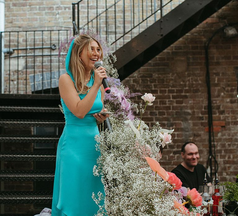 Bridesmaid/maid of honour in a bright turquoise dress and matching hair ribbon gives a speech at the reception 