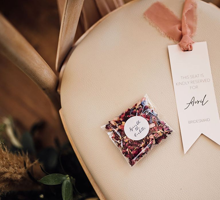 Dried petal confetti beside neutral toned wedding stationery tied with peach ribbon