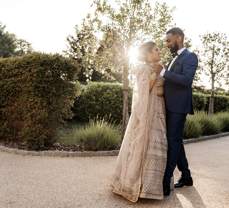 Bride wears gold embellished wedding dress whilst dancing with her groom during golden hour outdoors