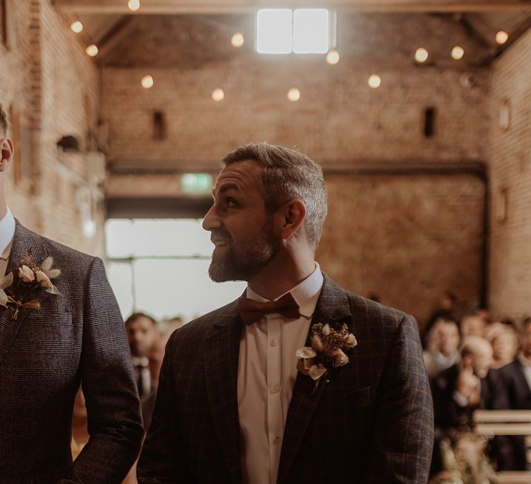 Groom and the best man stand at the altar with a grey checkered suit jacket with dried bunny grass buttonhole 