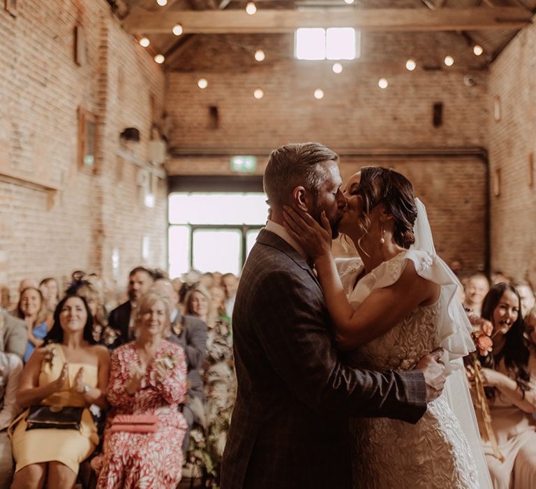 Bride and groom share their first kiss as a married couple at their rustic luxe barn wedding 