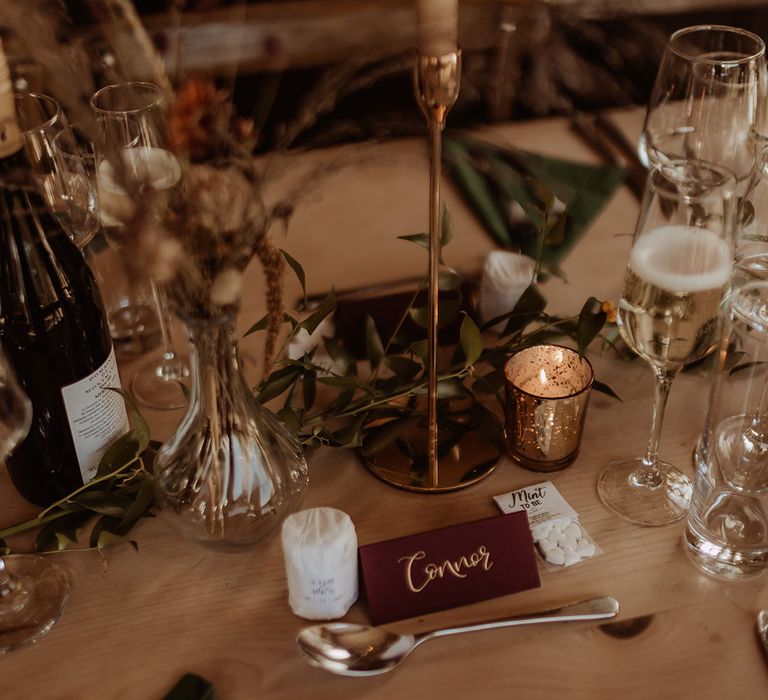 Scented candle wedding favours with a small pack of mints with neutral, red, and gold table decor 