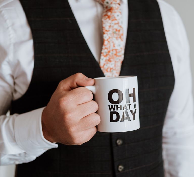 Groom holds novelty mug and wears black waistcoat with floral tie 