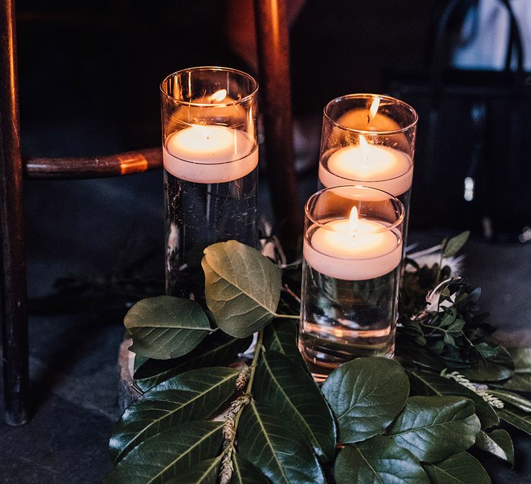 Hurricane vases filled with water and floating tea lights with foliage for aisle decor