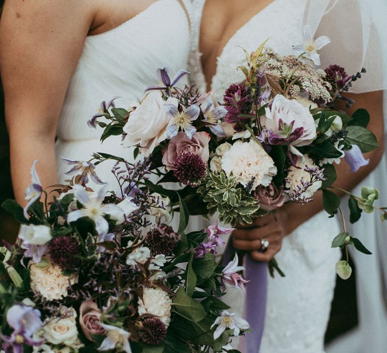 Matching bridal bouquets with white carnations, purple tulips, roses and foliage and lavender and white lace ribbon