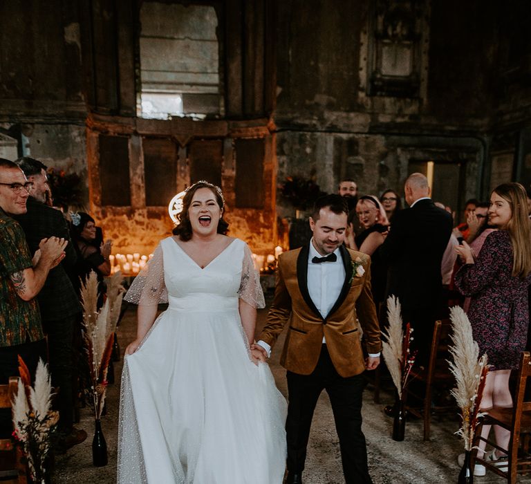 Bride and Groom walk up the aisle in coloured suit jacket and starry wedding dress