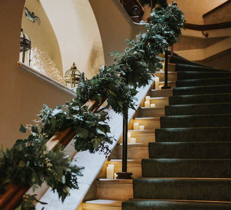 Decorative foliage wrapped around the bannister with pillar candles in glass hurricane vases 