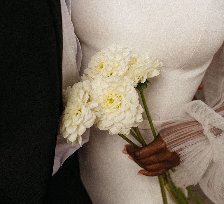 Bride and groom posing, holding a bunch of white dahlias at black-tie wedding with black and white table decorations