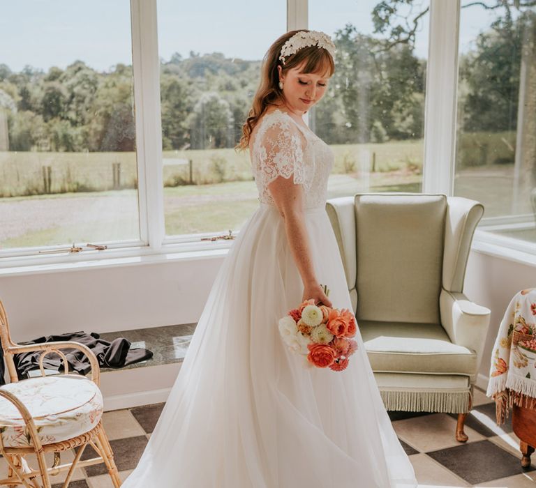 Bride wearing a tulle wedding dress with lace glittery sleeves with a pink and white wedding bouquet and white flower headband 