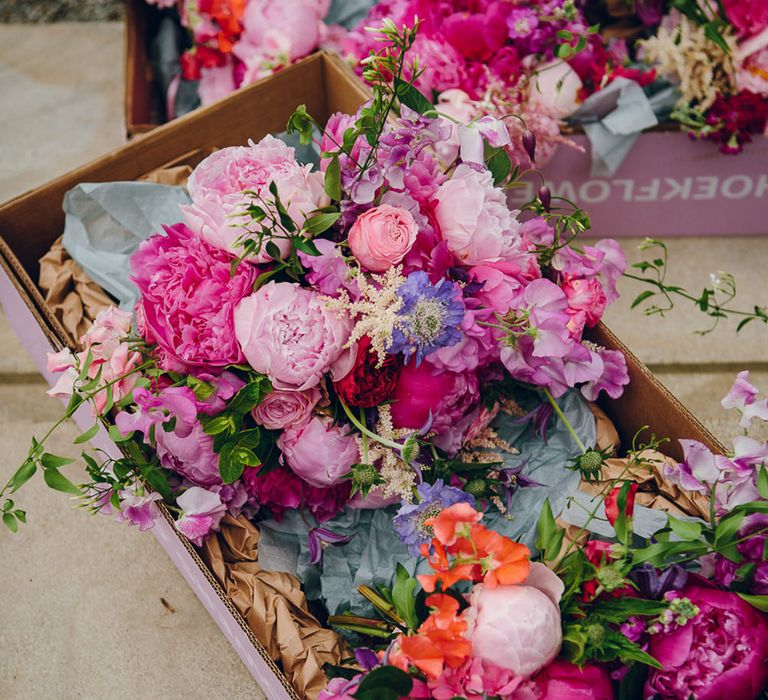 Pink floral bouquet with pink peonies, fuchsia roses, lilac sweet peas and green foliage in pink flower boxes