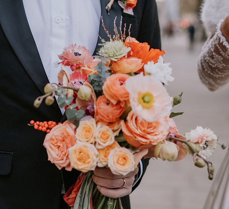 Bridal bouquet with light pink poppies, orange garden roses, eucalyptus, Christmas red berry garlands, dried flowers and sage green and orange ribbon