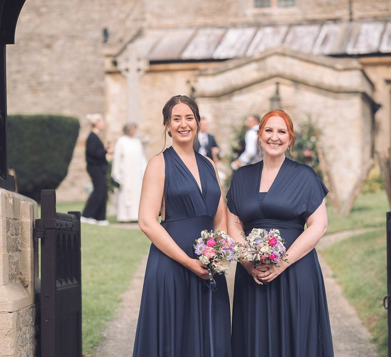 Bridesmaids in midnight blue satin dresses with pink and purple small round bouquet with the bride and groom's pet dog wearing a navy suit and bow tie 