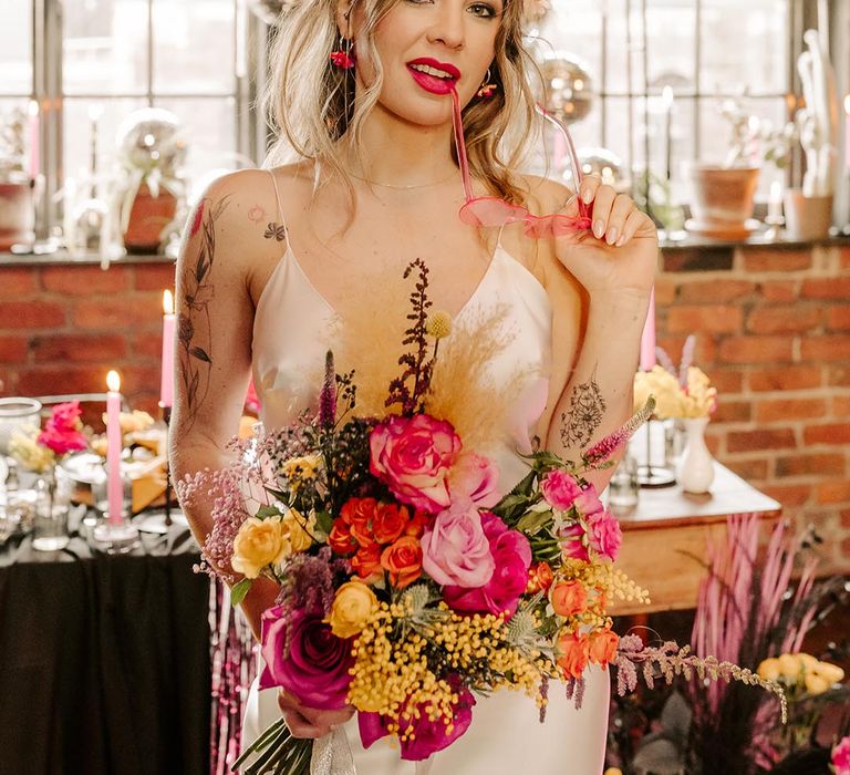 Bride in v-neck satin wedding dress, artistic flower crown, pink sheer sunglasses and pink garden rose, pampas grass, carnations, baby's-breath, dried flower and foliage bridal bouquet with sheer white lace ribbon 