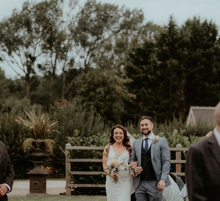 Bride is walked down the aisle by a man in a three piece grey suit with a blue tie and black waistcoat 