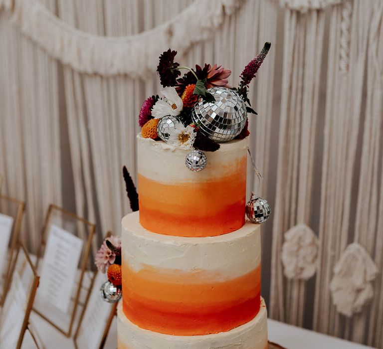 three tier buttercream wedding cake with white and orange ombre design and disco ball decor 