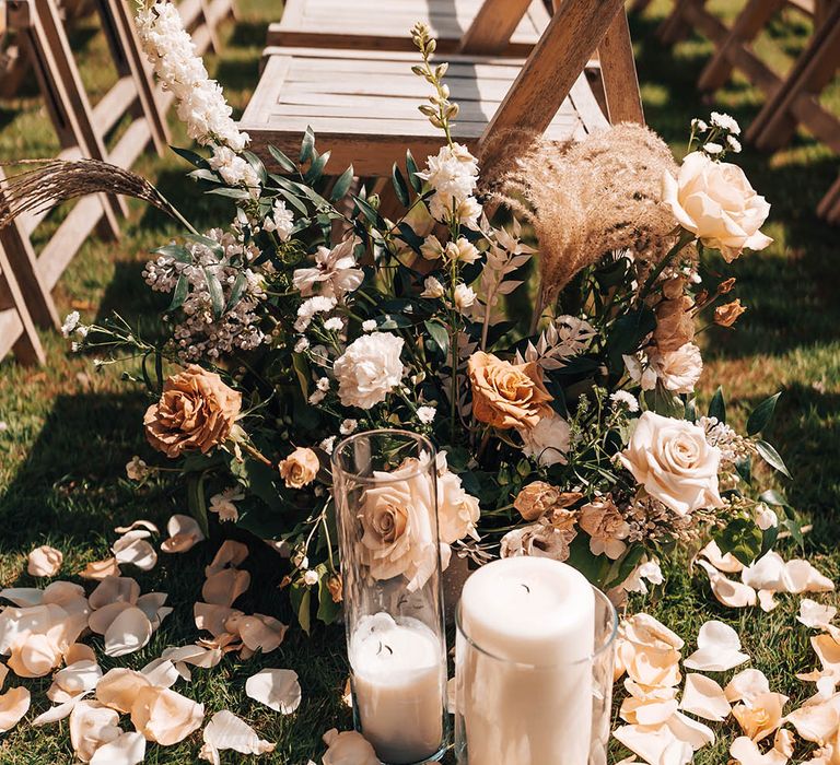 Boho luxe orange and cream wedding flower arrangement decorating the aisle with roses and rose petals on the floor with pillar candles 