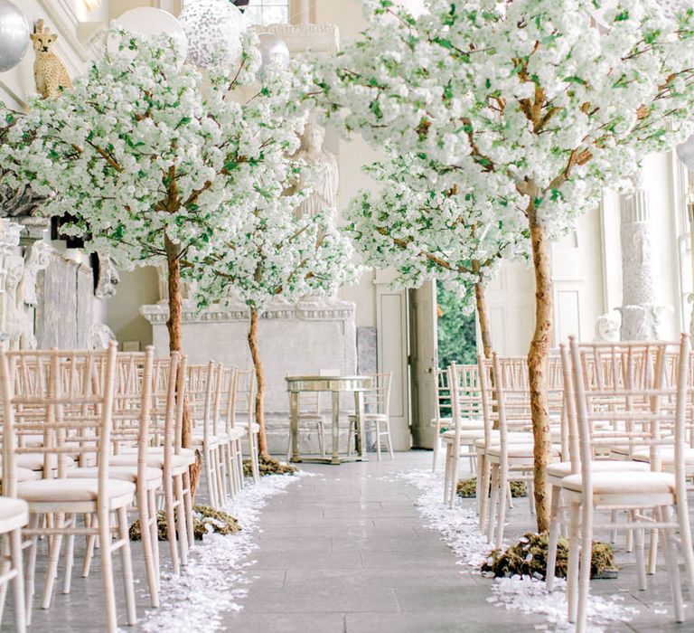 White flower petals line the aisle with tall tree indoor aisle decoration for a luxury wedding 