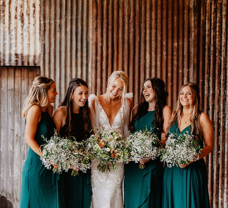 The bridesmaids in matching green bridesmaid dresses holding gypsophila bouquets with the bride in her fitted lace wedding dress for the rustic barn wedding 