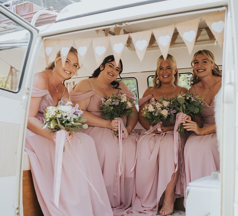 Bridesmaids in pink off the shoulder bridesmaid dresses holding their bouquets sitting in cream VW transportation 