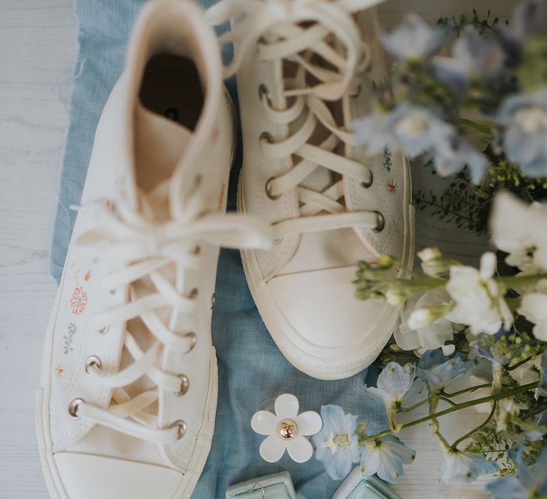 Embroidered white wedding converse with blue fabric, blue velvet jewellery boxes with silver jewellery and white and blue wedding flowers 