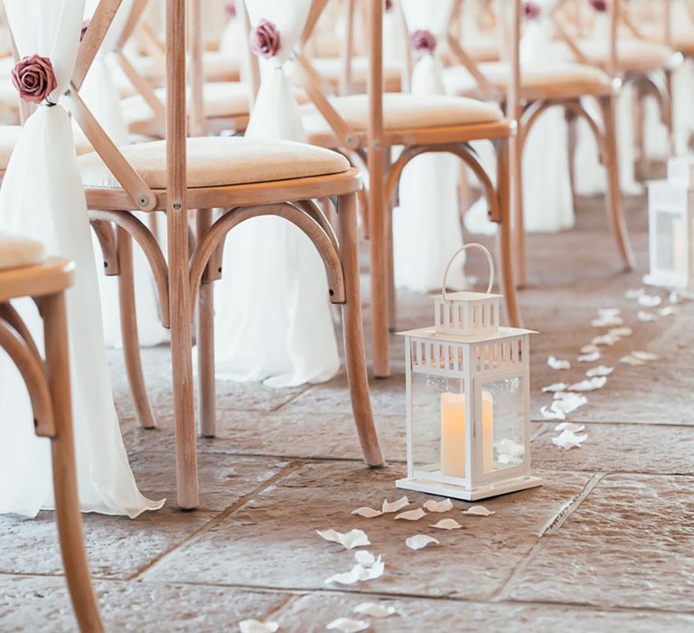 White wedding drapes tied with pink rose decorating the ceremony chairs with candles in lanterns and white rose petals 