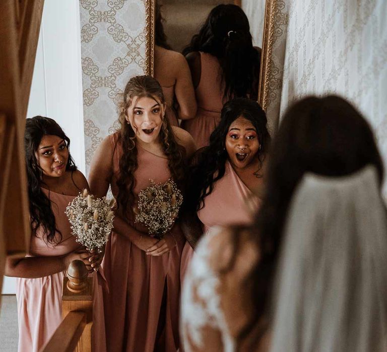 Bridesmaids in dusky pink one shoulder bridesmaids dresses holding dried flower bouquets seeing bride for the first time 