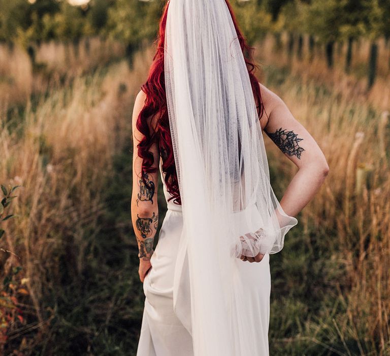 Bride in Halfpenny London wedding dress with veil and long red hair curled in mermaid style waves 