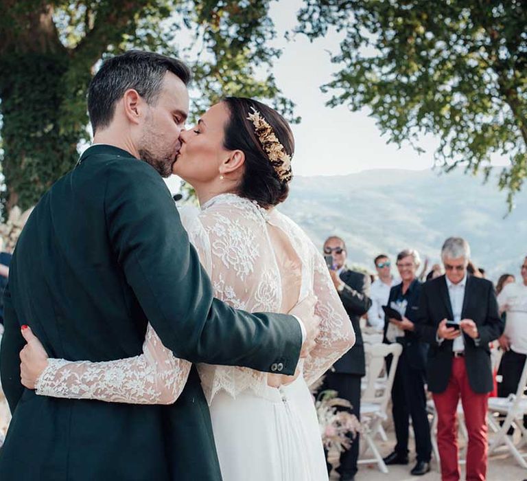 bride in a long sleeve lace wedding dress with dried flower crown embracing her husband 