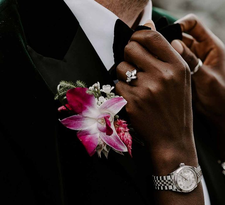 Bride in silver sparkly jewellery adjusting groom's tropical pink grooms boutonniere and bowtie on groom wearing bottle green velvet blazer 