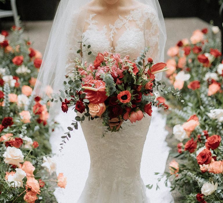 Bride holding large red wedding bouquet with poppies, roses and eucalyptus in long sleeve illusion lace Pronovias gown 