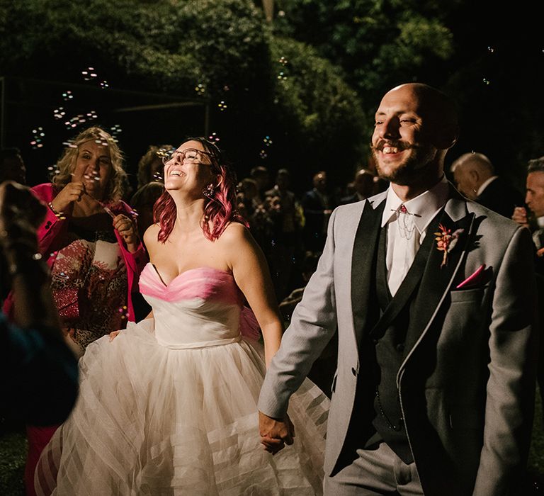 alternative bubble exit with bride in strapless wedding dress with layered skirt and groom in a light grey suit with dark lapel and waistcoat