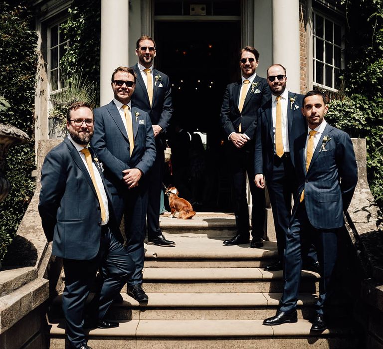 Groomsmen line the stairs of the wedding venue in navy suits 