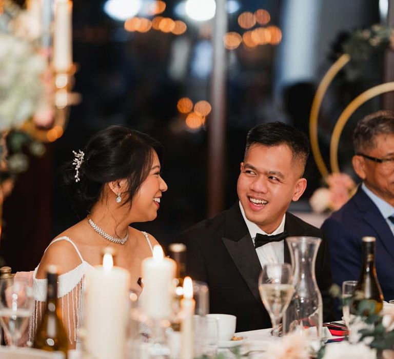 Bride in classic black tux smiling at bride in white slip wedding dress with tassels at Burmese wedding at Bron Eifion wedding venue