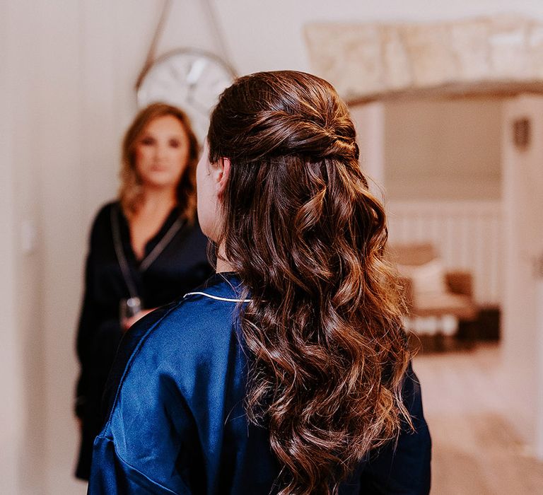 Bride in dark blue satin pyjamas with half up half down brown hair in waved hair style 