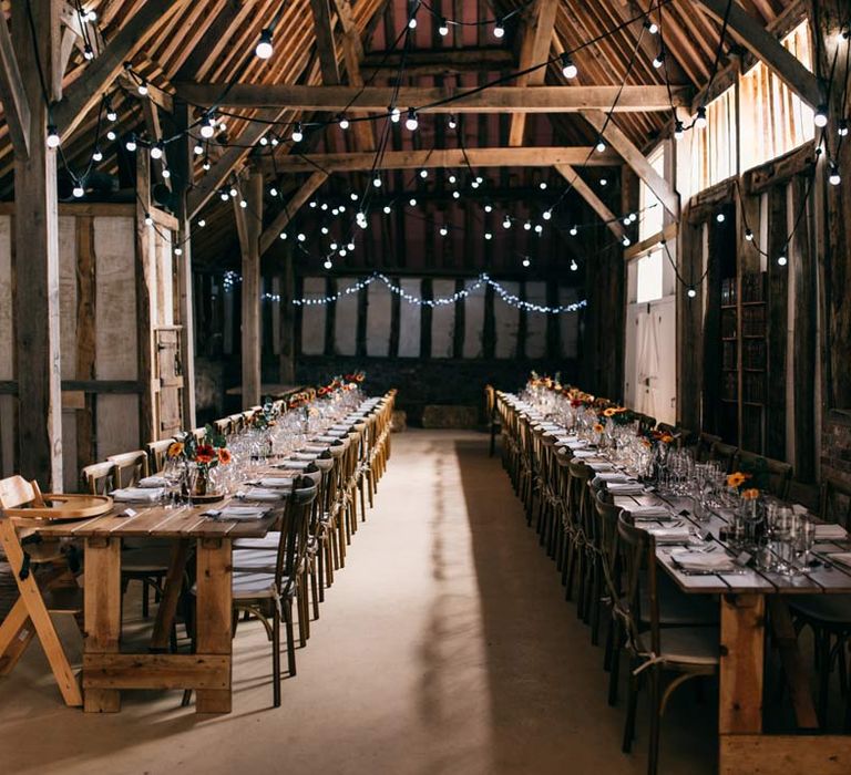 Templars Barn reception room with classic rustic wedding tablescape with floral centrepieces on wooden tree stumps, bookshelves with vintage books and hanging fairylights