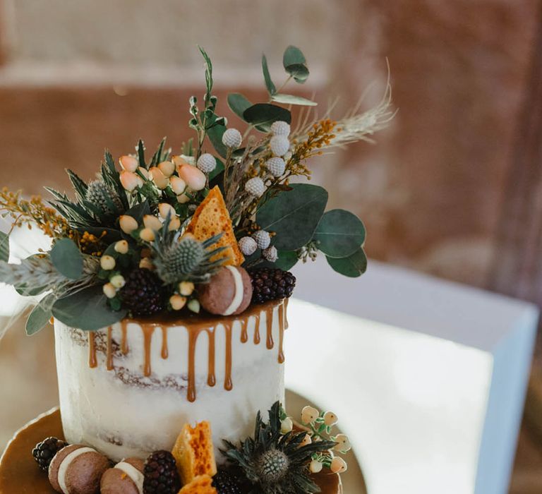 Caramel drip icing style on semi-naked frosted wedding cake decorated with natural style flowers and foliage 